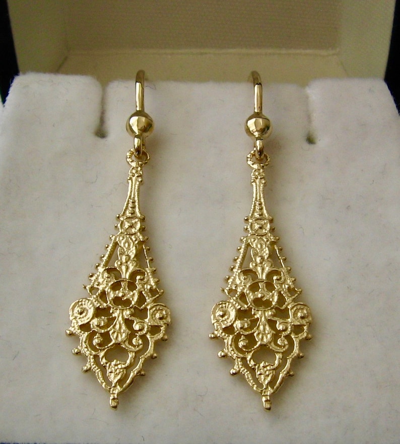 May include: A pair of gold filigree dangle earrings with a delicate, intricate design. The earrings are made of 14k gold and have a classic, elegant style.