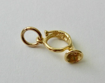 May include: A gold-colored charm in the shape of a French horn. The charm has a loop for attaching to a bracelet or necklace.