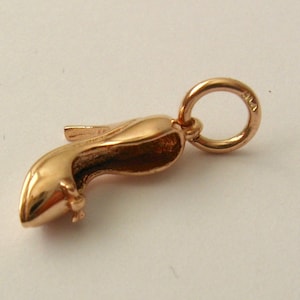 May include: A gold-toned charm in the shape of a high-heeled shoe. The charm has a loop at the top for attaching to a bracelet or necklace.