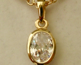 Op de afbeelding: Een gouden ketting met een hanger met een heldere ovale edelsteen.