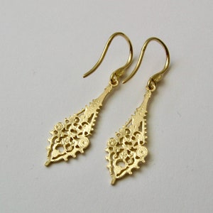 May include: A pair of gold dangle earrings with a delicate, intricate design. The earrings are shaped like a teardrop and feature a filigree pattern.