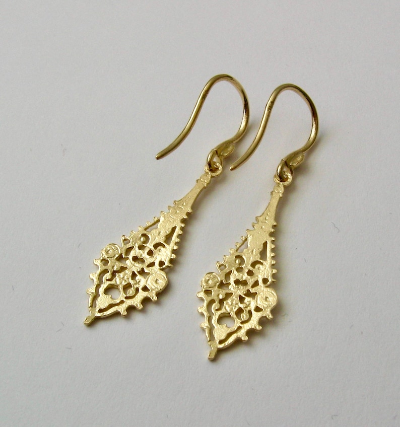 May include: A pair of gold dangle earrings with a delicate, intricate design. The earrings are shaped like a teardrop and feature a filigree pattern.