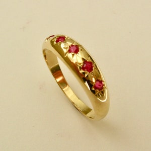 May include: A gold band ring with five red gemstones set in a row.