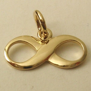 May include: A gold-coloured infinity symbol charm with a loop at the top for attaching to a necklace or bracelet. The charm is smooth and shiny, reflecting light. The design represents eternity and endless possibilities.
