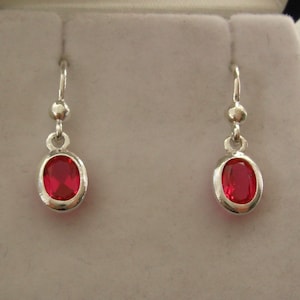 May include: A pair of silver dangle earrings with red oval-shaped gemstones.