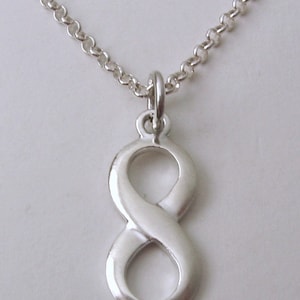 May include: A silver necklace with an infinity symbol pendant. The pendant, a figure eight shape, hangs from a fine chain. The necklace is shown against a plain backdrop.