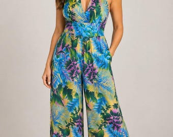 Könnte beinhalten: Ein ärmelloser Jumpsuit mit Neckholder-Ausschnitt und einem lebendigen tropischen Blattmuster in Blau-, Grün-, Gelb- und Violetttönen. Das Kleidungsstück hat einen tiefen V-Ausschnitt, eine betonte Taille und eine weite Hose mit Seitentaschen.