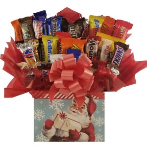 May include: A festive candy bouquet featuring a variety of wrapped chocolate bars and candies, arranged in a red paper-lined box. The box is decorated with a large pink bow and a vintage illustration of Santa Claus holding a gift.