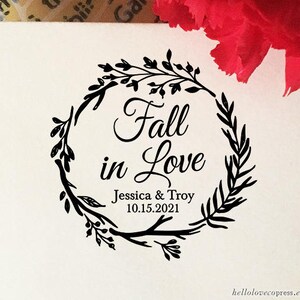May include: A black and white stamp with a wreath of leaves and the text "Fall in Love" with the names Jessica & Troy and the date 10.15.2021.