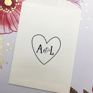 May include: White paper favor bag with a black heart design and the initials "A & L" inside the heart.