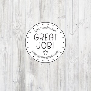 May include: A black and white circular sticker with the text "Mrs. Hendrix says GREAT JOB! Keep up the good work!" and a star in the center. The sticker is on a white wood background.