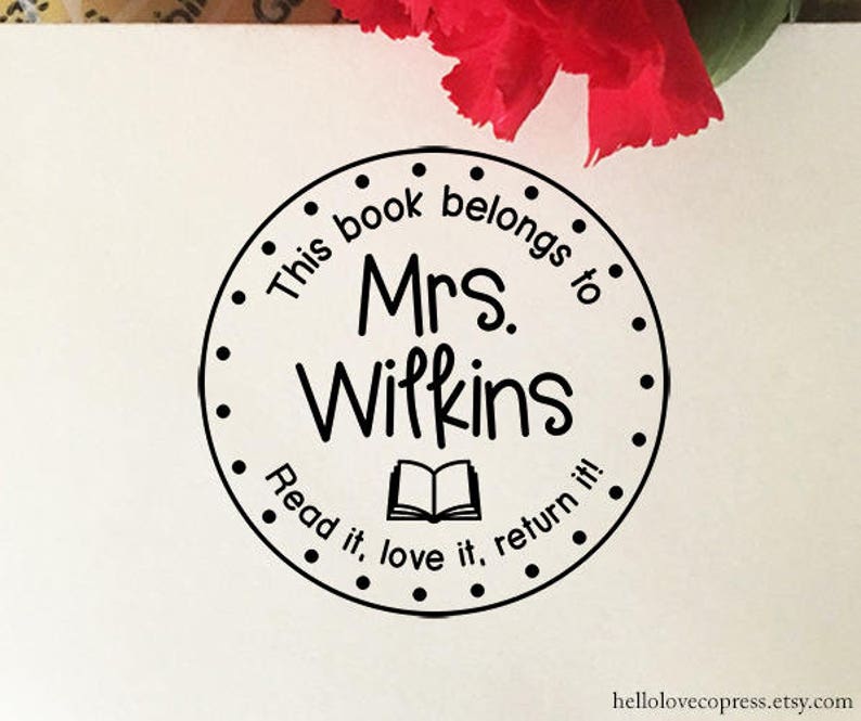 Puede incluir: Sello redondo en blanco y negro con el texto "This book belongs to Mrs. Wilkins Read it, love it, return it!" y una imagen de un libro abierto.