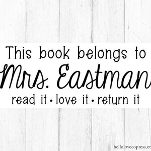 May include: Black and white text on a white wood background. The text reads "This book belongs to Mrs. Eastman read it. love it. return it."
