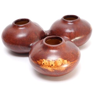 May include: Three brown ceramic pots with a design of a pueblo village on one of the pots.