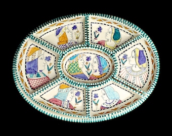 May include: An oval ceramic serving dish with six sections. Each section features a hand-painted design of a couple in profile, with a floral motif. The dish is decorated with a green and gold border.