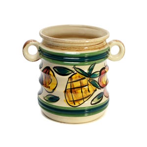 May include: A ceramic vase with a cream-colored base, adorned with hand-painted fruit designs, including a yellow pineapple. The vase has two loop handles and is accented with green and brown stripes. The vase is approximately 7 inches tall.
