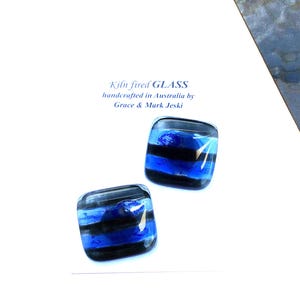 May include: Two square, kiln-fired glass pieces with a blue and black striped design. The glass is handcrafted in Australia. The text on the image reads "Kiln fired GLASS handcrafted in Australia by Grace & Mark Jeski."