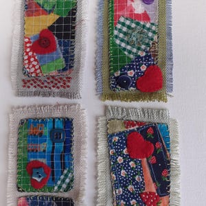 May include: Four handmade fabric patches with a patchwork design. Each patch features a unique combination of patterned fabrics, buttons, and felt hearts. The patches are rectangular with frayed edges, showcasing a rustic, handcrafted aesthetic.