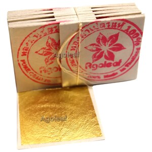 Puede incluir: Una pila de hojas de oro, cada hoja est&aacute; envuelta en papel blanco con un sello rosa que dice "Agoleaf 100% Pure Gold Leaf".