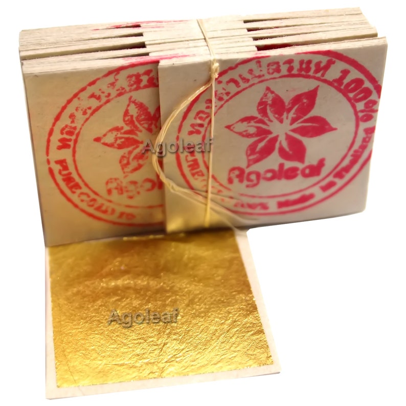 Puede incluir: Una pila de hojas de oro, cada hoja est&aacute; envuelta en papel blanco con un sello rosa que dice "Agoleaf 100% Pure Gold Leaf".
