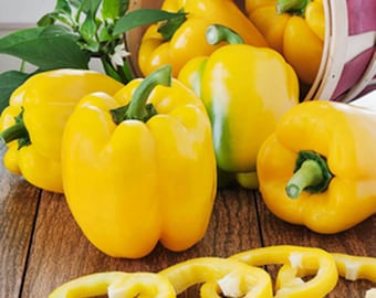 May include: A collection of bright yellow bell peppers, both whole and sliced, are arranged on a wooden surface. A basket with a red and white striped pattern contains several whole peppers. Green stems and leaves provide a fresh contrast.