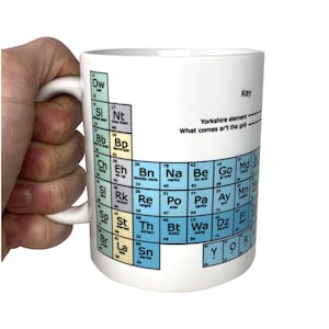 May include: White ceramic mug with a periodic table design featuring Yorkshire slang words instead of chemical elements. The mug has a black handle and the text "Yorkshire element What comes ar't the gob" is printed on the mug.
