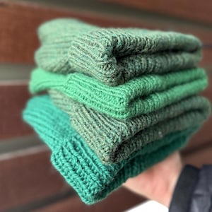 May include: Stack of four knitted hats in shades of green, from dark green to light green.