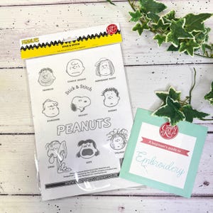 Op de afbeelding: Een Peanuts Stick & Stitch borduurpakket met stripfiguren als Snoopy en Charlie Brown. Inclusief een beginnersgids voor borduren. De verpakking heeft een gele kop en een witte achtergrond.