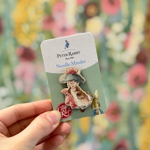 Op de afbeelding: Een Peter Rabbit naaldhouder met een illustratie van een konijn met een hoed en een tas. De kaart leest "The World of Peter Rabbit" en "Needle Minder". Het logo van The Crafty Kit Co. is ook zichtbaar.