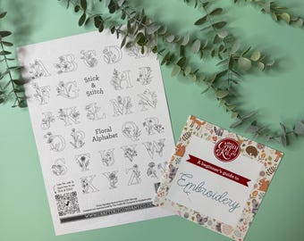 May include: A white sheet of paper with a floral alphabet printed on it. The alphabet is in black and white and each letter is surrounded by small flowers. The paper is titled "Stick & Stitch Floral Alphabet". Below the alphabet is a QR code and the website "www.craftykitcompany.co.uk". A small booklet titled "A beginner's guide to Embroidery" is on top of the paper. The booklet has a colourful design with animals and flowers.