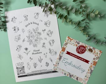 May include: A white sheet of paper with a black and white floral design of numbers 1 through 9 and an ampersand. The paper has the text "Stick & Stitch" and "Floral Numbers" printed on it. A small card with a colourful floral design and the text "A beginner's guide to Embroidery" is on top of the paper.