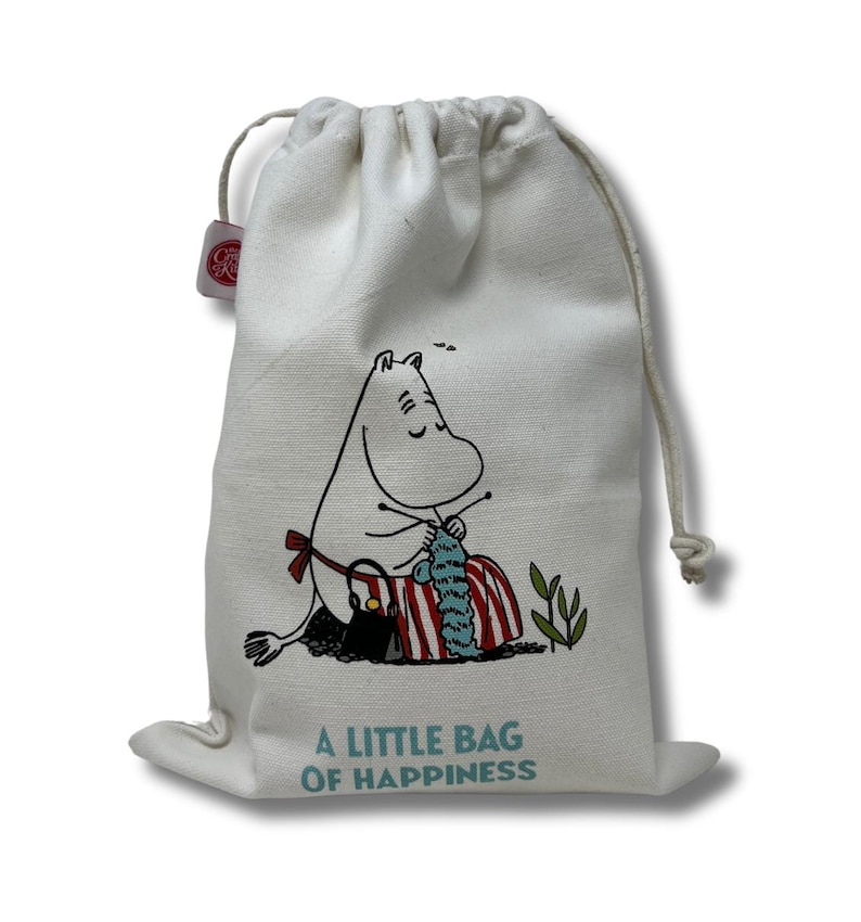 May include: A white canvas drawstring bag with a cartoon illustration of a white hippopotamus knitting. The bag has the text "A little bag of happiness" printed on the front.