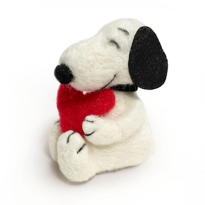 Peut inclure: Une figurine Snoopy en feutre blanc tenant un cœur rouge. La figurine a des oreilles noires, un nez noir et un collier noir. La figurine Snoopy est assise et a les yeux fermés, ce qui lui donne une apparence paisible.
