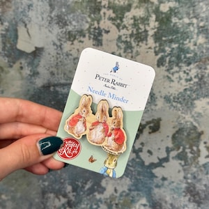 May include: A Peter Rabbit needle minder set. The card features three wooden rabbit figures in red jackets. Text includes "The World of Peter Rabbit" and "Needle Minder". The Crafty Kit Co. logo is visible.