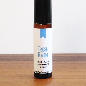 May include: A brown glass roll-on bottle with a black cap and a white label. The label says "Fresh Rain" and "Fresh Rain Dew Drops & Mist" with a blue and white graphic.