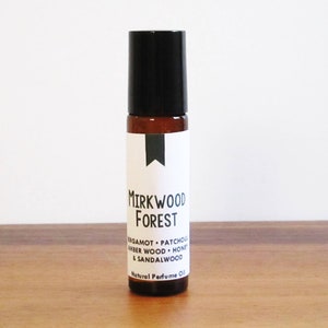 May include: A brown glass roll-on bottle with a black cap and a white label that reads "Mirkwood Forest" and lists the ingredients "Bergamot - Patchouli - Amber Wood - Honey & Sandalwood". The label also says "Natural Perfume Oil".