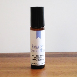 May include: A brown glass roller bottle with a black cap and a white label. The label has the text "EDNA ST. VINCENT MILLA FIG DEW DROPS LAVENDER & APPLE BLOSSOM Natural Perfume Oil 03/17".