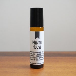 Puede incluir: Un peque&ntilde;o frasco de vidrio &aacute;mbar con un tap&oacute;n de rodillo negro. La etiqueta es blanca con texto negro que dice "NINTH HOUSE" y enumera las notas de la fragancia: "CANDIED GINGER, SALT, CARAMEL, SAGE, LIME, LAVENDER, TOBACCO LEAF, PALO SANTO, SAFFRON, AMBER & CEDARWOOD". El texto "Natural Perfume Oil / 10ml" tambi&eacute;n est&aacute; en la etiqueta.