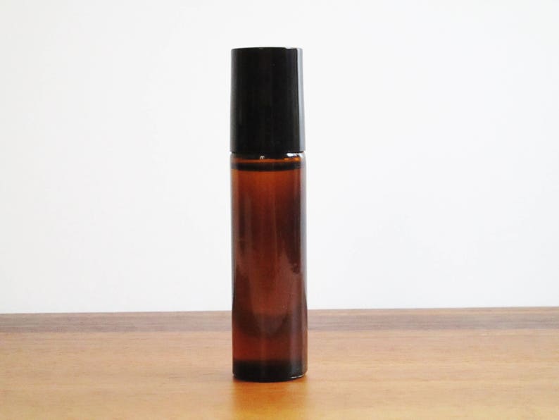 May include: A brown glass roller bottle with a black lid. The bottle is filled with a clear liquid.