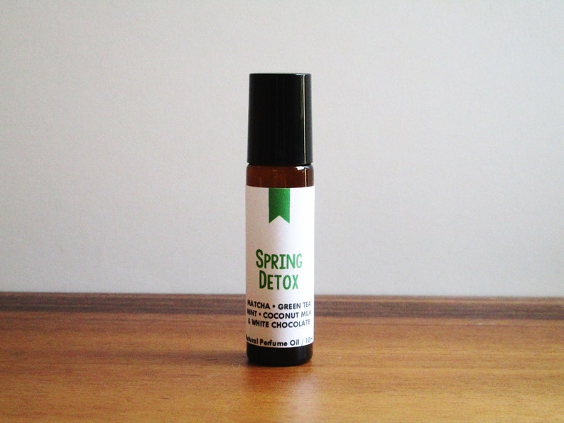 May include: A brown glass roller bottle with a black cap and a white label that says "Spring Detox" with the ingredients listed below: Matcha, Green Tea, Mint, Coconut Milk, White Chocolate.