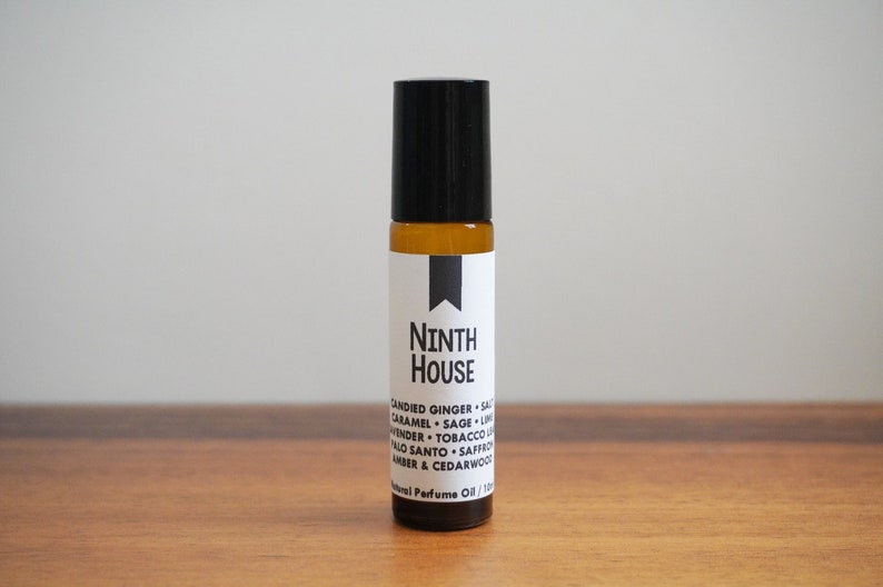 Puede incluir: Un peque&ntilde;o frasco de vidrio &aacute;mbar con un tap&oacute;n de rodillo negro. La etiqueta es blanca con texto negro que dice "NINTH HOUSE" y enumera las notas de la fragancia: "CANDIED GINGER, SALT, CARAMEL, SAGE, LIME, LAVENDER, TOBACCO LEAF, PALO SANTO, SAFFRON, AMBER & CEDARWOOD". El texto "Natural Perfume Oil / 10ml" tambi&eacute;n est&aacute; en la etiqueta.