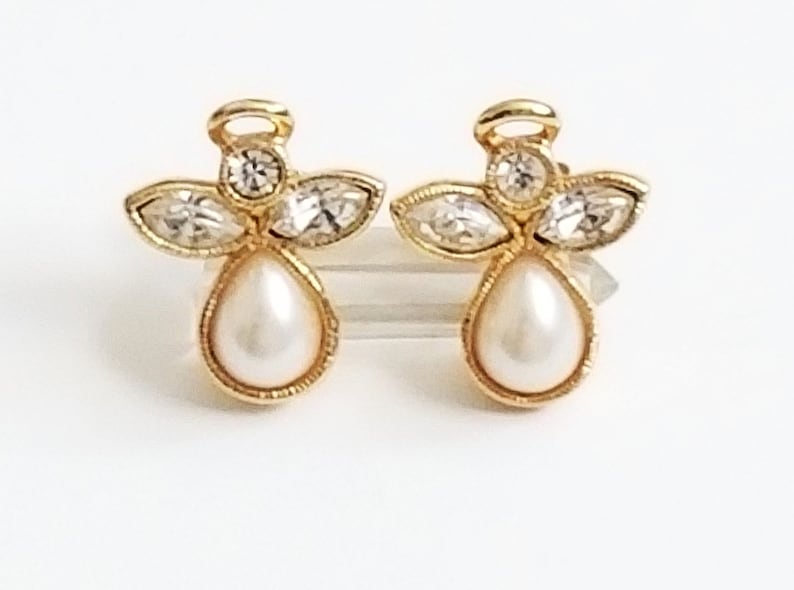 May include: A pair of gold angel-shaped earrings with a pearl drop and clear crystal accents.