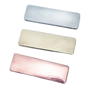 May include: Three rectangular metal bars in silver, gold, and rose gold. Each bar has rounded corners and a brushed metal finish. The bars are arranged vertically against a white background.
