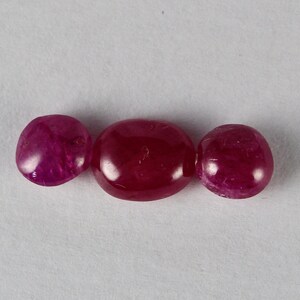 Könnte beinhalten: Drei runde, rote Rubin-Edelsteine. Die Edelsteine sind glatt und poliert.