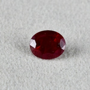 May include: A deep red oval-shaped gemstone with facets.