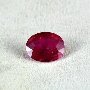 May include: A deep red oval-shaped gemstone with facets.