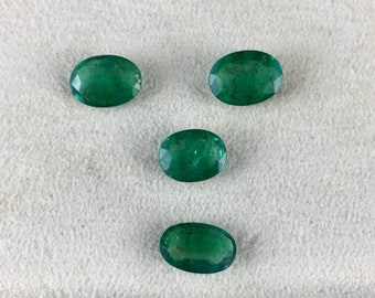 May include: Five oval-shaped emerald gemstones on a white surface. The gemstones are a vibrant green color and have a smooth, polished finish.