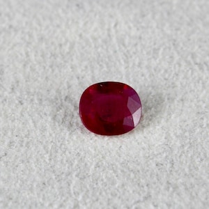 May include: A deep red oval-shaped gemstone with a faceted cut.