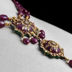 Pu&ograve; includere: Una collana d'oro con un ciondolo di rubino e diamanti. Il ciondolo &egrave; composto da due rubini rotondi circondati da diamanti pi&ugrave; piccoli e pietre verdi.