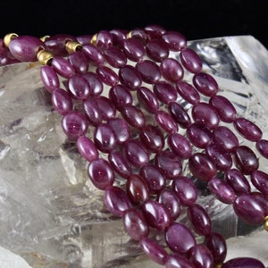 Pu&ograve; includere: Una collana multifilo realizzata con perline di rubino ovali di colore viola scuro con distanziatori dorati.